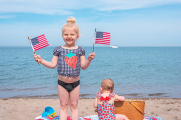 Cute little blonde girl at the beach holding American flags