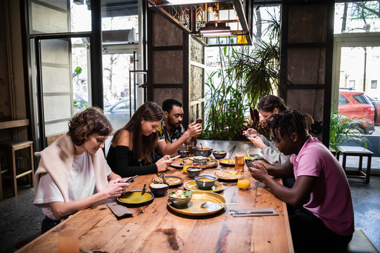 A international group of students sharing food in a cafe and usi - Powered by Adobe
