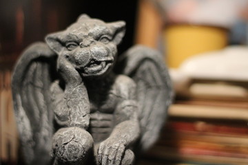 Statue of a small thinking gargoyle sitting on a bookshelf