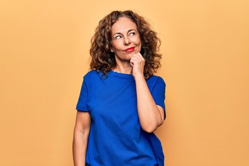 Middle age beautiful woman wearing casual t-shirt standing over isolated yellow background thinking...