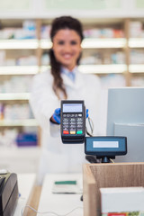Female pharmacist holding credit card swipe machine.