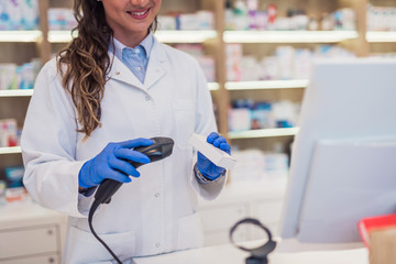 Female pharmacist register a product price on her system. She is using bar code reader.