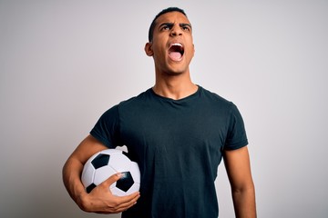 Handsome african american man playing footbal holding soccer ball over white background angry and...