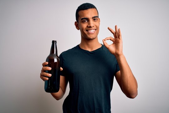 Young Handsome African American Man Drinking Bottle Of Beer Over White Background Doing Ok Sign With Fingers, Excellent Symbol