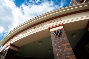 Entrance to a building built in memory of fallen service people in past wars, against a lovely blue sky with clouds.