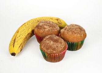 One very ripe banana and three homemade banana muffins in green and red paper holders on a white background.