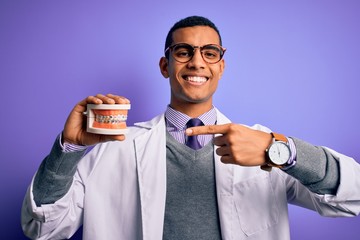 Young handsome african american dentist man holding denture teeth with dental braces very happy pointing with hand and finger
