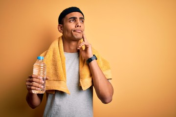 Young handsome african american sportsman wearing towel drinking bottle of water serious face...