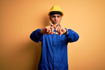 Young handsome african american worker man wearing blue uniform and security helmet Rejection expression crossing fingers doing negative sign