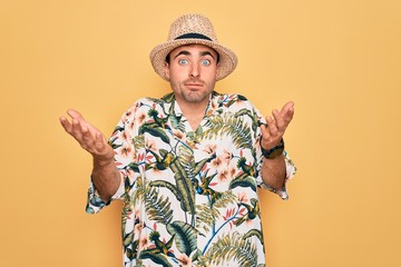 Young handsome man with blue eyes on vacation wearing summer florar shirt and hat clueless and...