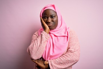 Young african american plus size woman wearing muslim hijab over isolated pink background thinking looking tired and bored with depression problems with crossed arms.