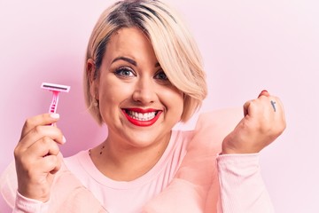 Young beautiful blonde plus size woman holding depilation razor over isolated pink background screaming proud, celebrating victory and success very excited with raised arm