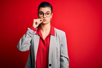 Young beautiful brunette businesswoman wearing jacket and glasses over red background mouth and...