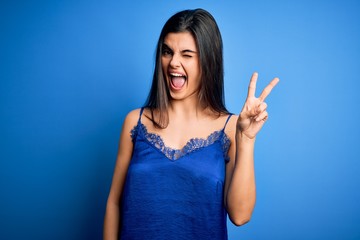 Young beautiful brunette woman wearing elegant and comfortable blue lingerie underwear smiling with happy face winking at the camera doing victory sign. Number two.