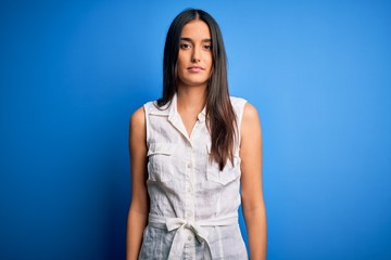 Young beautiful brunette woman wearing casual dress over isolated blue background Relaxed with serious expression on face. Simple and natural looking at the camera.