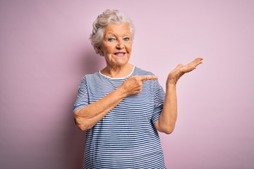 Senior beautiful grey-haired woman wearing casual t-shirt over isolated pink background amazed and smiling to the camera while presenting with hand and pointing with finger.