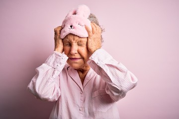 Senior beautiful woman wearing sleep mask and pajama over isolated pink background suffering from headache desperate and stressed because pain and migraine. Hands on head.