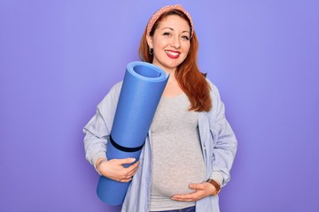 Young beautiful redhead pregnant woman expecting baby holding mat to do prenatal exercise with a happy face standing and smiling with a confident smile showing teeth