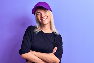 Young beautiful blonde woman wearing t-shirt and purple cap over isolated background happy face smiling with crossed arms looking at the camera. Positive person.