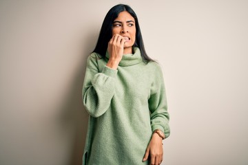 Young beautiful hispanic woman wearing green winter sweater over isolated background looking stressed and nervous with hands on mouth biting nails. Anxiety problem.