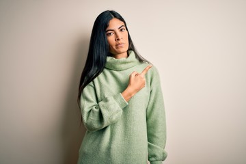 Young beautiful hispanic woman wearing green winter sweater over isolated background Pointing with hand finger to the side showing advertisement, serious and calm face
