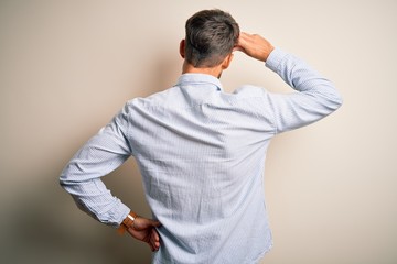 Young handsome man with beard wearing striped shirt standing over white background Backwards thinking about doubt with hand on head