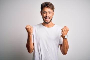 Fototapeta premium Young handsome man with beard wearing casual t-shirt standing over white background celebrating surprised and amazed for success with arms raised and open eyes. Winner concept.