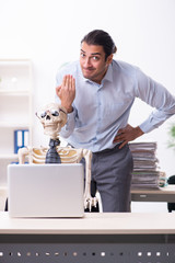 Young male employee and skeleton in the office