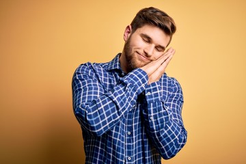 Young blond businessman with beard and blue eyes wearing shirt over yellow background sleeping tired dreaming and posing with hands together while smiling with closed eyes.