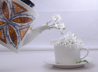 Teapot serving small flowers on a white cup.