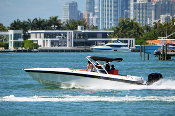 Obraz premium White motor boat with black trim powered by a single outboard engine cruising on Biscayne Bay off Miami Beach,Florida