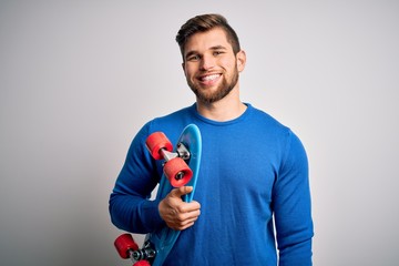 Young blond skeater man with beard and blue eyes holding skate over white background with a happy face standing and smiling with a confident smile showing teeth © Krakenimages.com