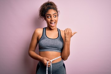 Young african american sporty girl controlling weight using tape measure on waist pointing and...