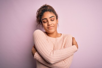 Young beautiful african american girl wearing casual sweater standing over pink background Hugging...