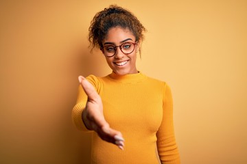 Young beautiful african american girl wearing sweater and glasses over yellow background smiling...