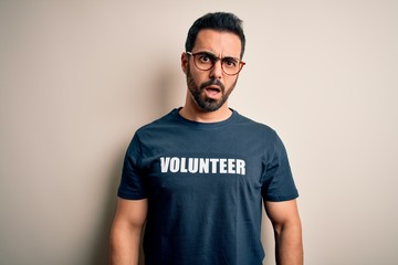 Handsome man with beard wearing t-shirt with volunteer message over white background In shock face, looking skeptical and sarcastic, surprised with open mouth