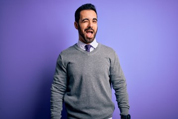 Obraz premium Handsome businessman with beard wearing casual tie standing over purple background winking looking at the camera with sexy expression, cheerful and happy face.