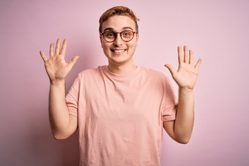 Young handsome redhead man wearing casual t-shirt standing over isolated pink background showing and pointing up with fingers number ten while smiling confident and happy.