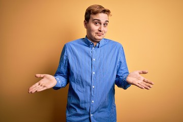 Young handsome redhead man wearing casual striped shirt over isolated yellow background clueless...