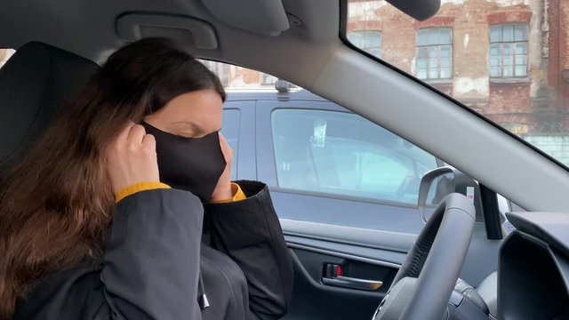 Woman driver in medical face mask cleaning hands with antibacterial sanitizer spray behind the wheel of her car during COVID-19 coronavirus pandemic.