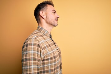 Young handsome man wearing casual shirt standing over isolated yellow background looking to side, relax profile pose with natural face with confident smile.