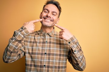 Young handsome man wearing casual shirt standing over isolated yellow background smiling cheerful showing and pointing with fingers teeth and mouth. Dental health concept.