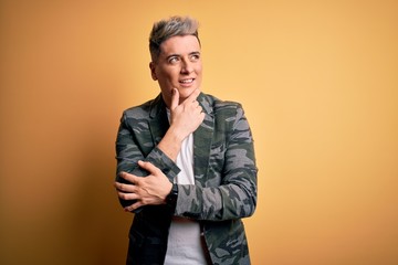 Young handsome modern man wearing business jacket standing over yellow isolated background with hand on chin thinking about question, pensive expression. Smiling with thoughtful face. Doubt concept.