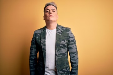 Young handsome modern man wearing business jacket standing over yellow isolated background Relaxed with serious expression on face. Simple and natural looking at the camera.