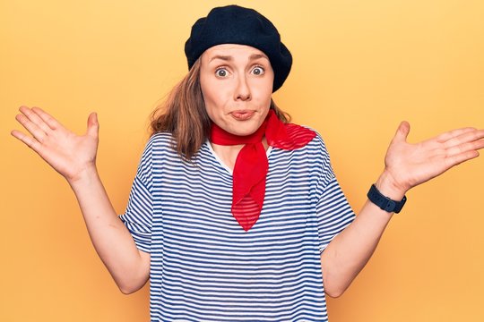 Young beautiful blonde woman wearing french fashion style with scarf and beret clueless and confused with open arms, no idea and doubtful face.