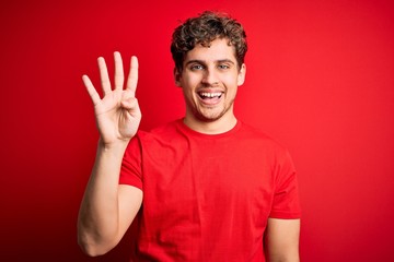 Young blond handsome man with curly hair wearing casual t-shirt over red background showing and pointing up with fingers number four while smiling confident and happy.
