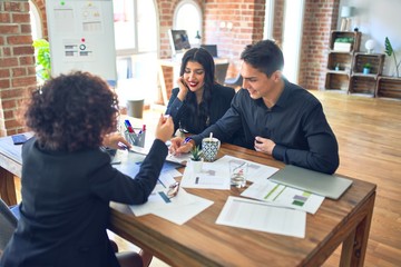 Young beautiful couple applying for mortgage. Sitting smiling happy meeting with real state agent considering mortgage loan at bank