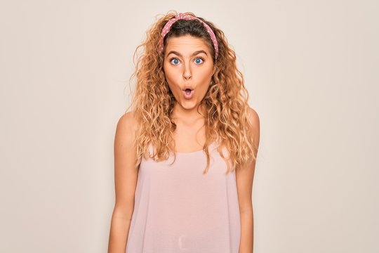 Young beautiful woman with blue eyes wearing casual t-shirt and diadem over pink background afraid and shocked with surprise expression, fear and excited face.