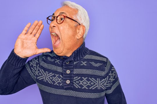 Middle age senior grey-haired man wearing glasses and winter sweater over purple background shouting and screaming loud to side with hand on mouth. Communication concept.