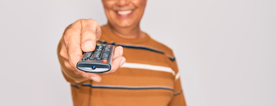 Middle age senior grey-haired man using tv remote control watching television with a happy face standing and smiling with a confident smile showing teeth